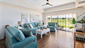 A spacious living room with a large window, a ceiling fan, and a wooden floor. - Golf Course View Condo w/ Pool Access, Near Disney (Reunion)