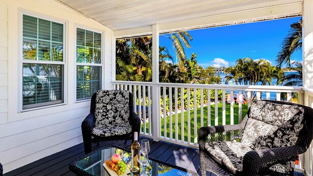 A covered outdoor seating area with two wicker chairs, a glass table, and a view of a tropical landscape. - Bayfront Villa:  Dock, Walk to Beach and Bridge Street (Bradenton Beach)