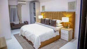 A modern bedroom with a large bed, bedside lamps, a wardrobe, and a small table with a plant. - Luxenest T1 (Lekki)