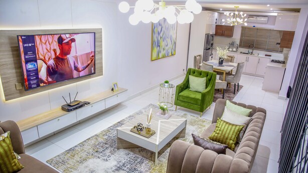 A modern living room with a flat-screen TV, a green armchair, a brown sofa, and a coffee table. - Luxenest T1 (Lekki)