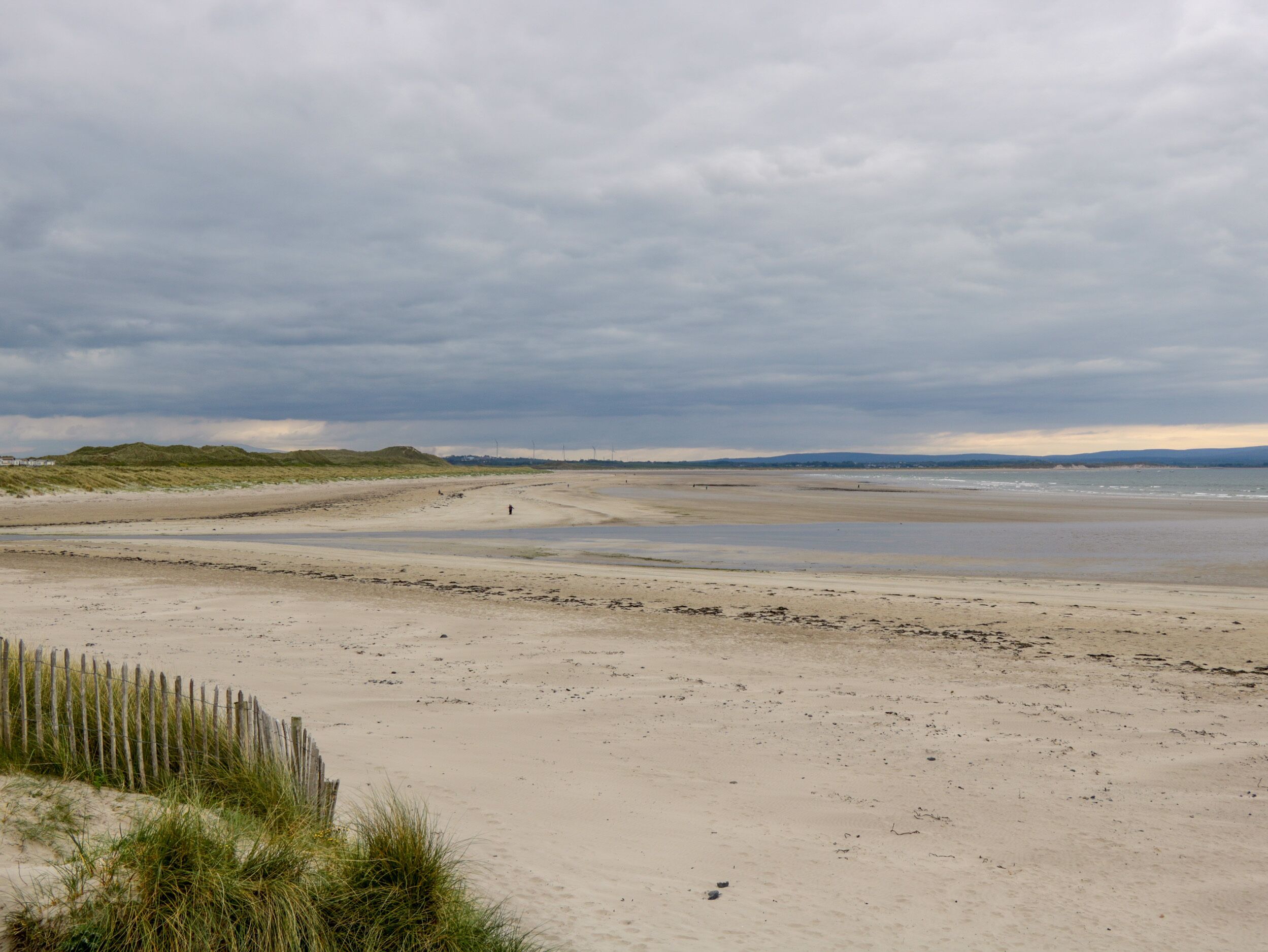 A sandy beach with dunes and a wooden fence.