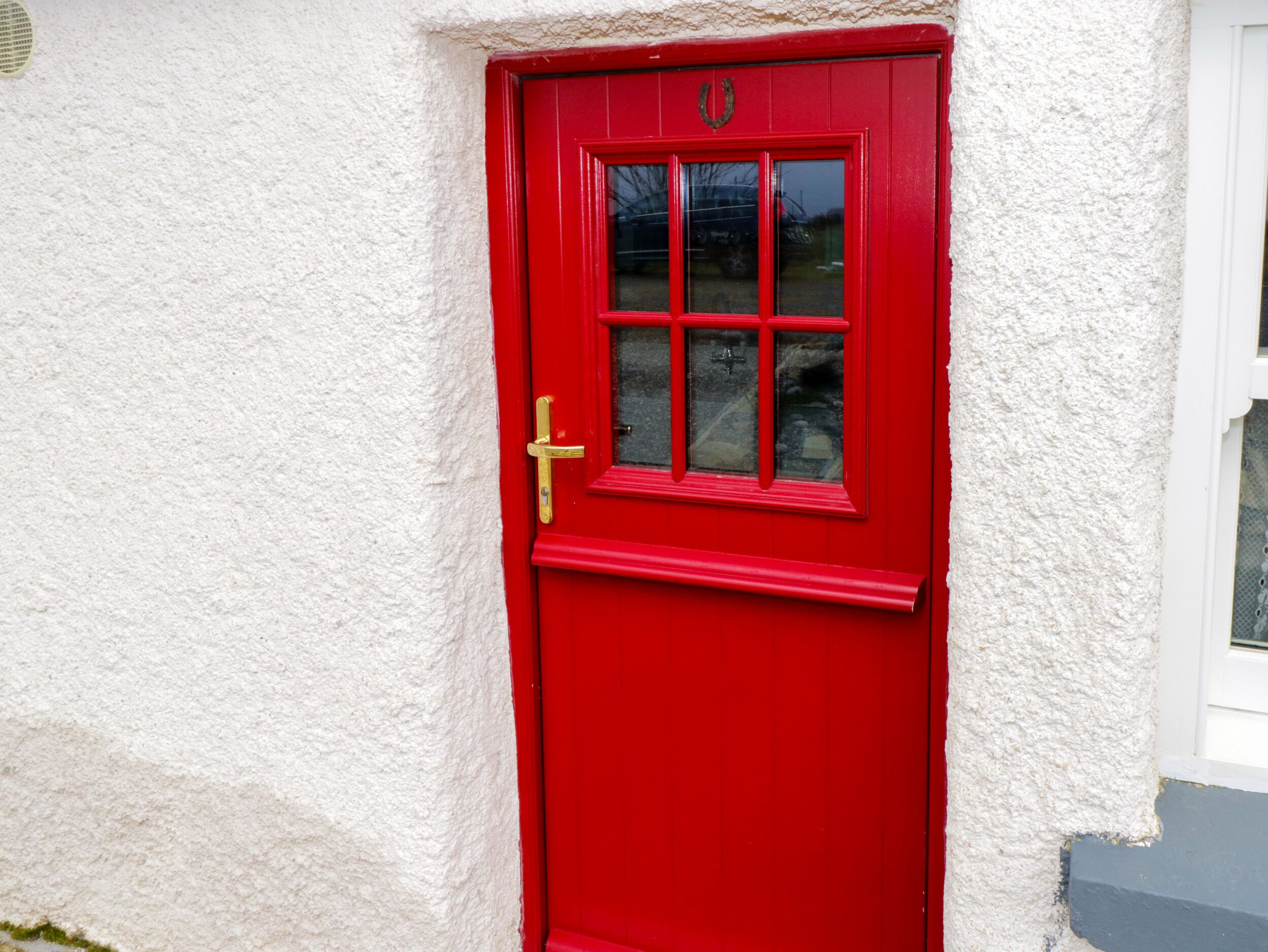 Une porte rouge avec une poignée dorée et des panneaux de verre, encadrée dans un mur blanc à texture.