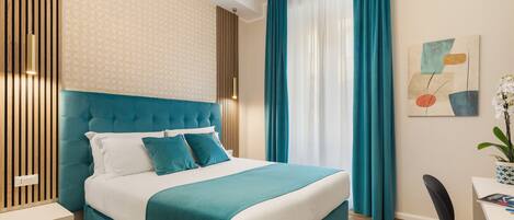 Una habitación de hotel moderna con una cama tapizada en color aguamarina, una mesita de noche blanca y un escritorio con una silla.