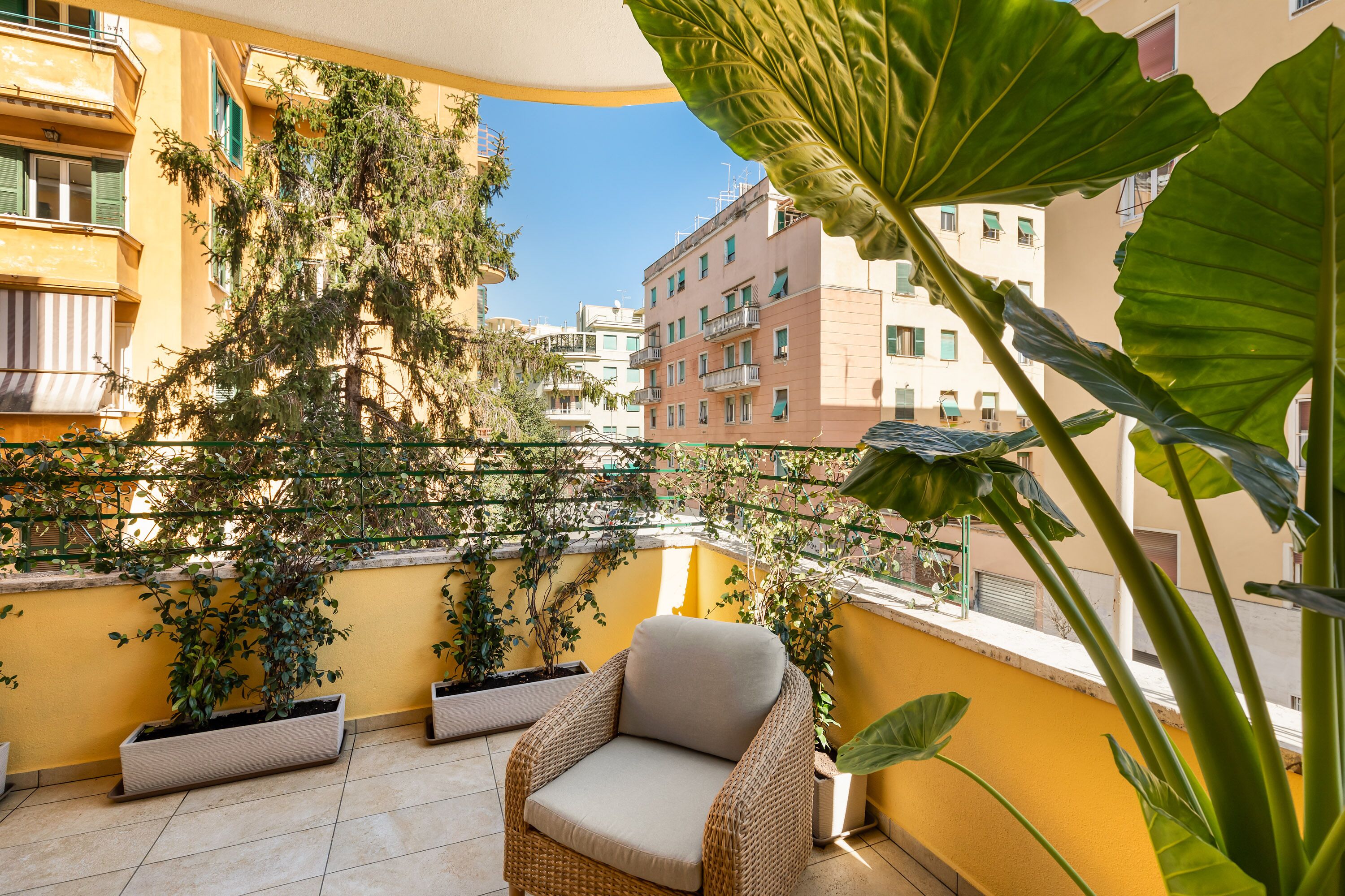 A balcony with a wicker chair, potted plants, and a view of buildings.