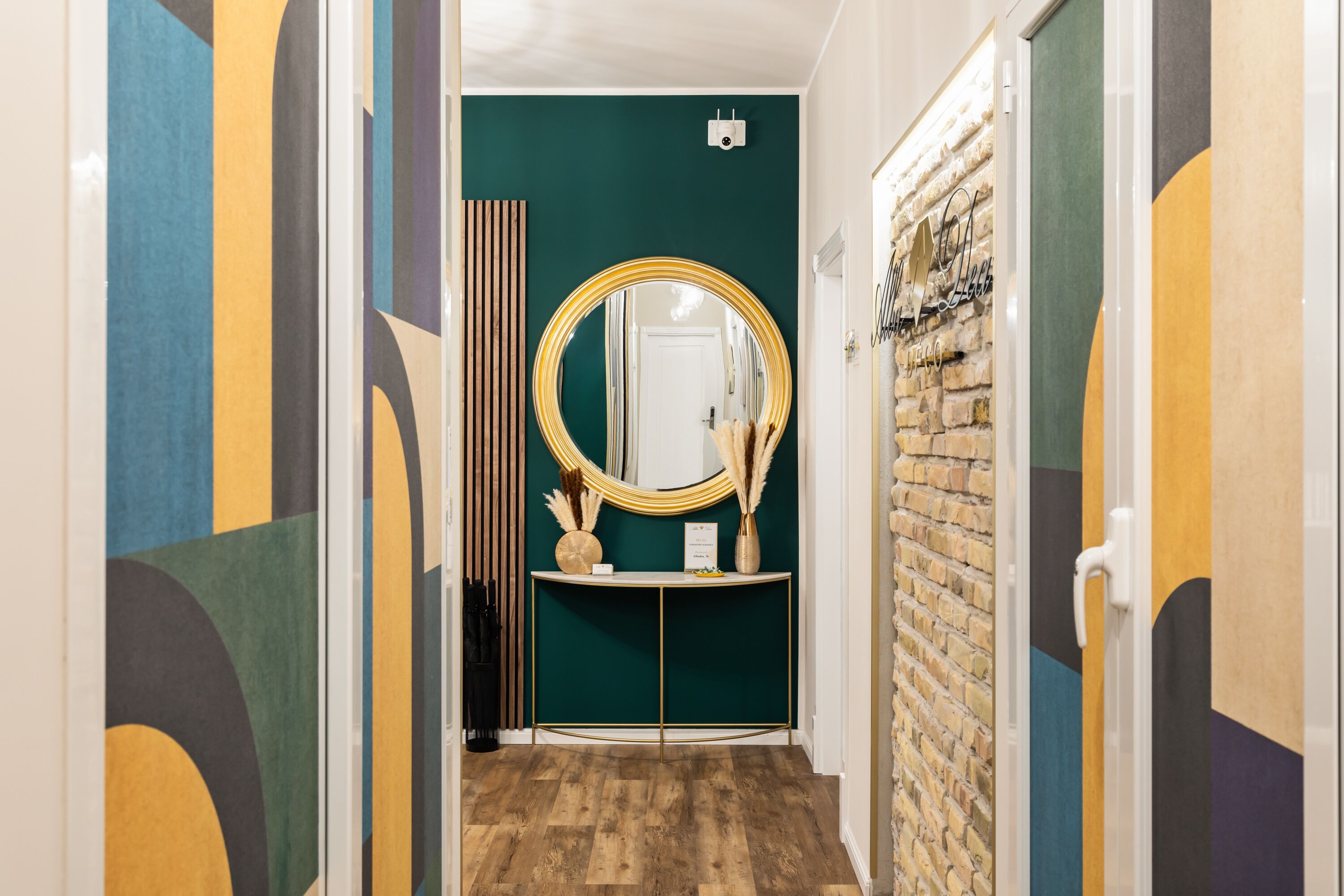 Un pasillo con pared verde, un espejo redondo, una consola y una pared de ladrillo.