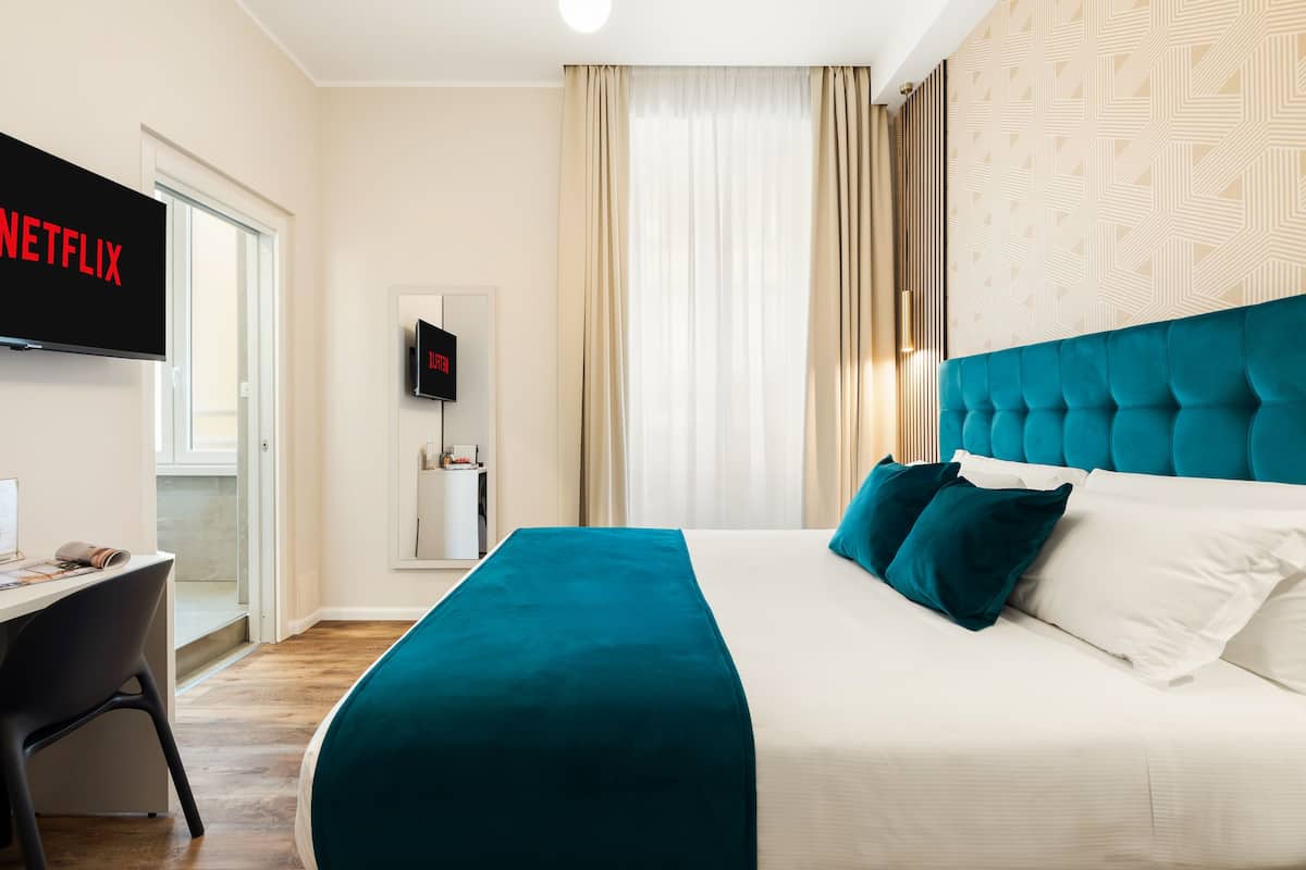 Una habitación de hotel con cama, escritorio, televisor y puerta.