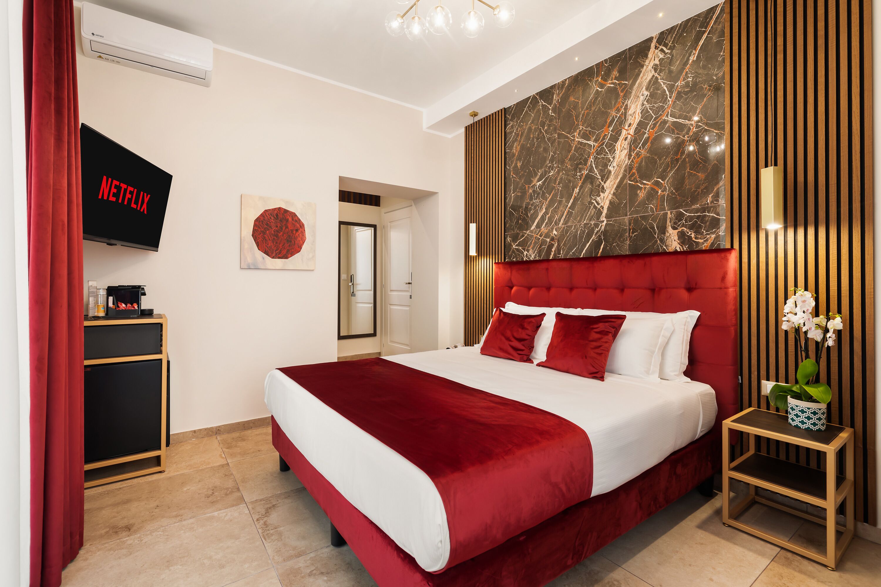 A modern hotel room with a large bed, a TV mounted on the wall, a red curtain, and a marble accent wall.
