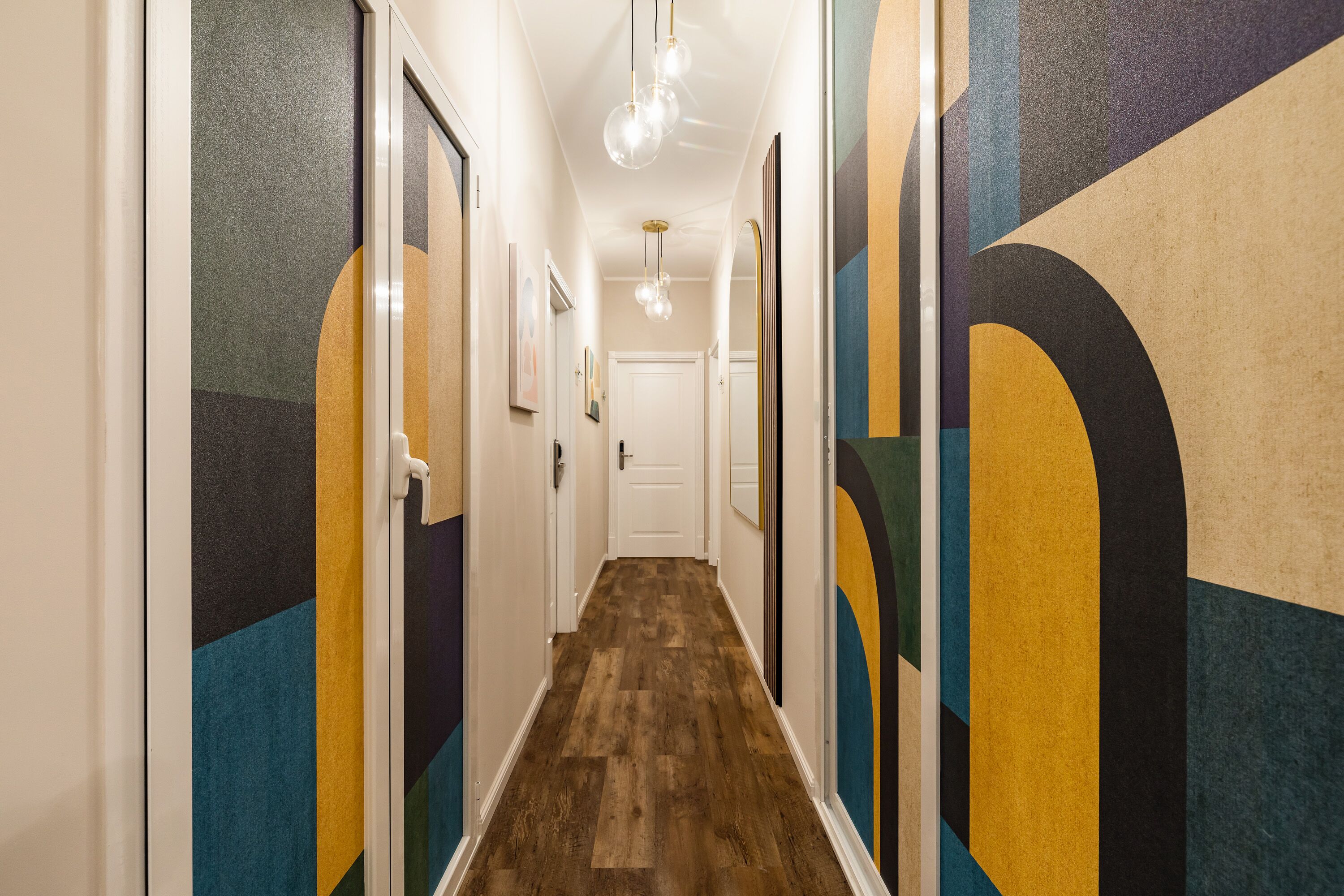 A hallway with a wooden floor, white walls, and colorful geometric wall art.