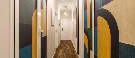 A hallway with a wooden floor, white walls, and colorful geometric wall art.