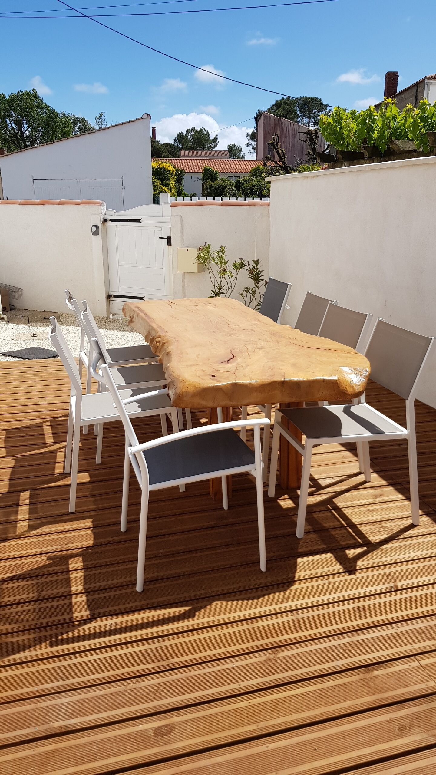 A wooden deck with a table and chairs, surrounded by white walls and a garden.