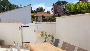 A wooden deck with a table and chairs, surrounded by white walls and a garden. - Au Calme, Centre La Tranche-sur-mer, 200m Commerces et Rues Animées, 300m Plage (La Tranche-sur-Mer)