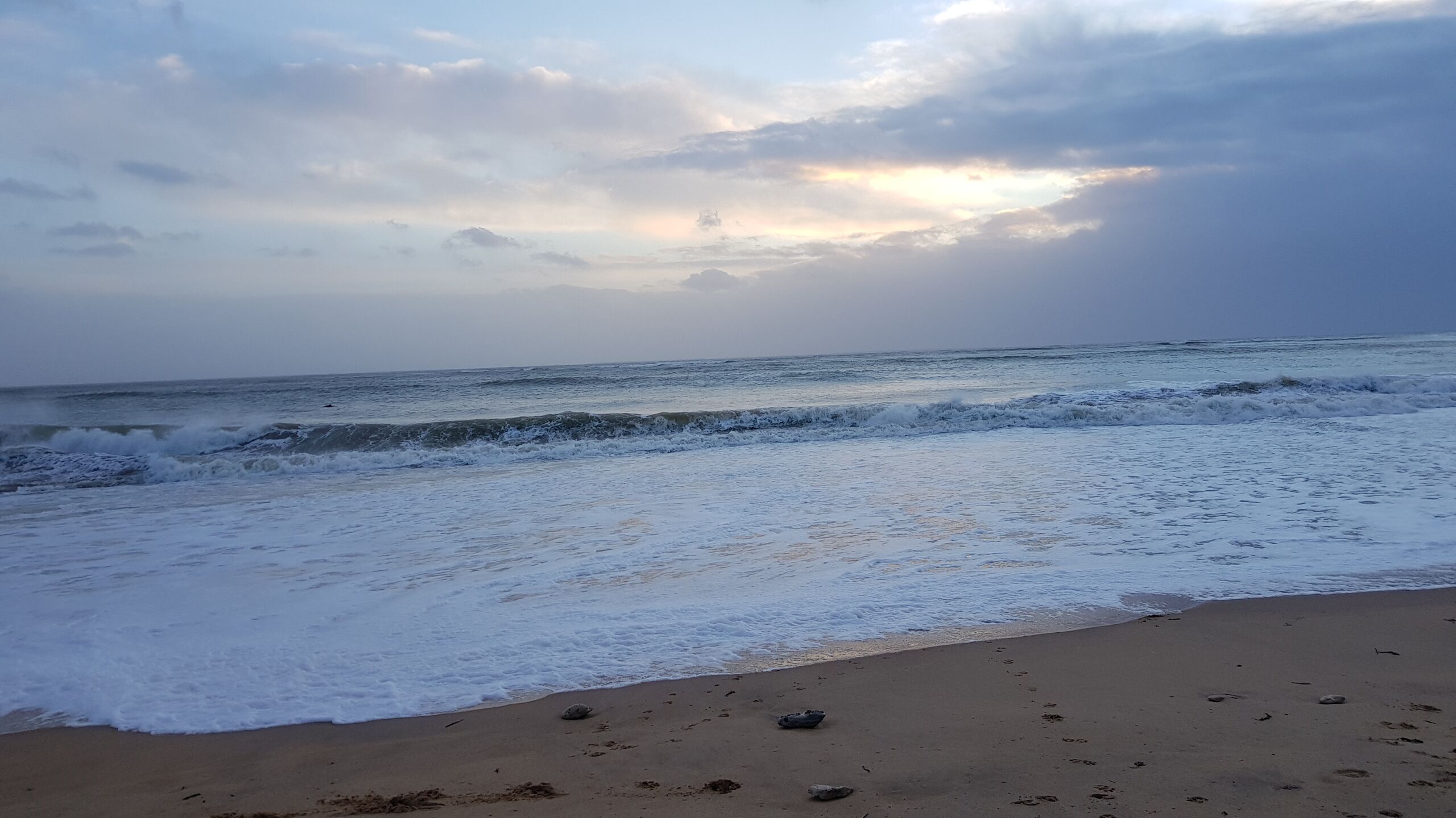 A beach with waves, a clear sky, and a sunset.