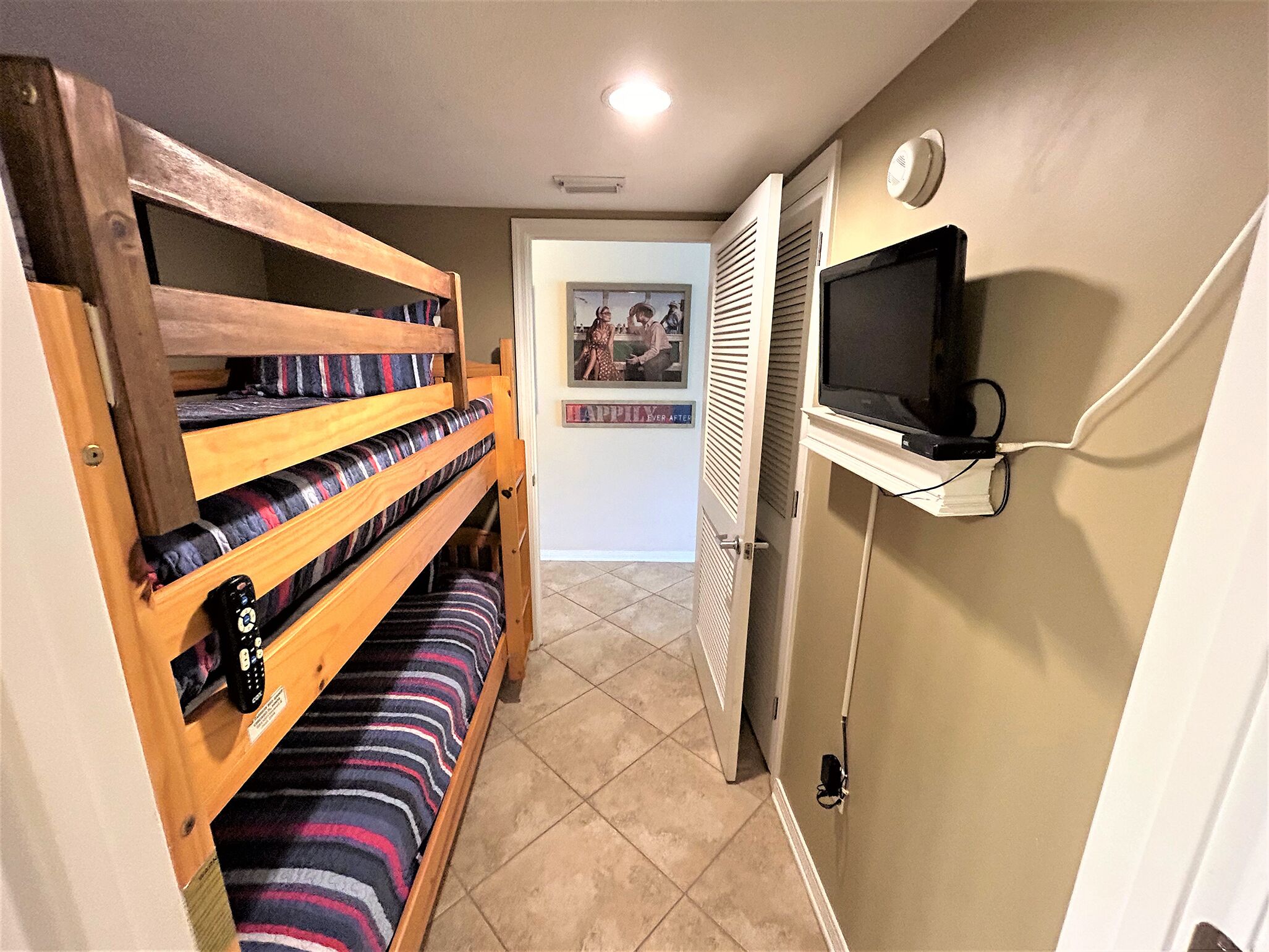 Una habitación con literas, un televisor montado en la pared y una puerta que da a otra habitación.