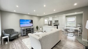 Un salon moderne avec un canapé gris, un téléviseur et une petite table blanche.