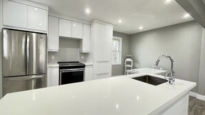 Une cuisine moderne dotée d’appareils électroménagers en acier inoxydable, de meubles blancs et d’un grand îlot central équipé d’un évier et d’un robinet.