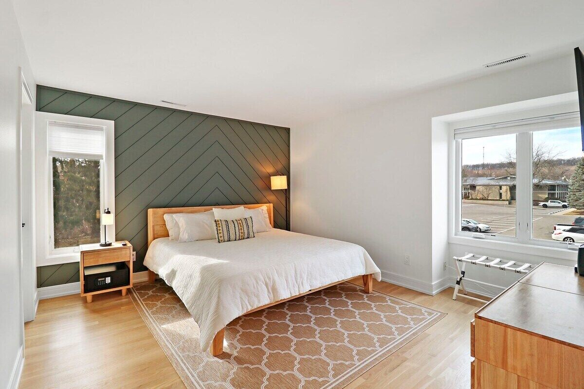 A bedroom with a bed, a nightstand, a lamp, a window, and a view of the outside.