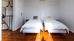 A room with two beds, wooden flooring, a staircase, and a hanging light fixture. - Maison Calme et Confortable à 10 Minutes de Paris (Alfortville)