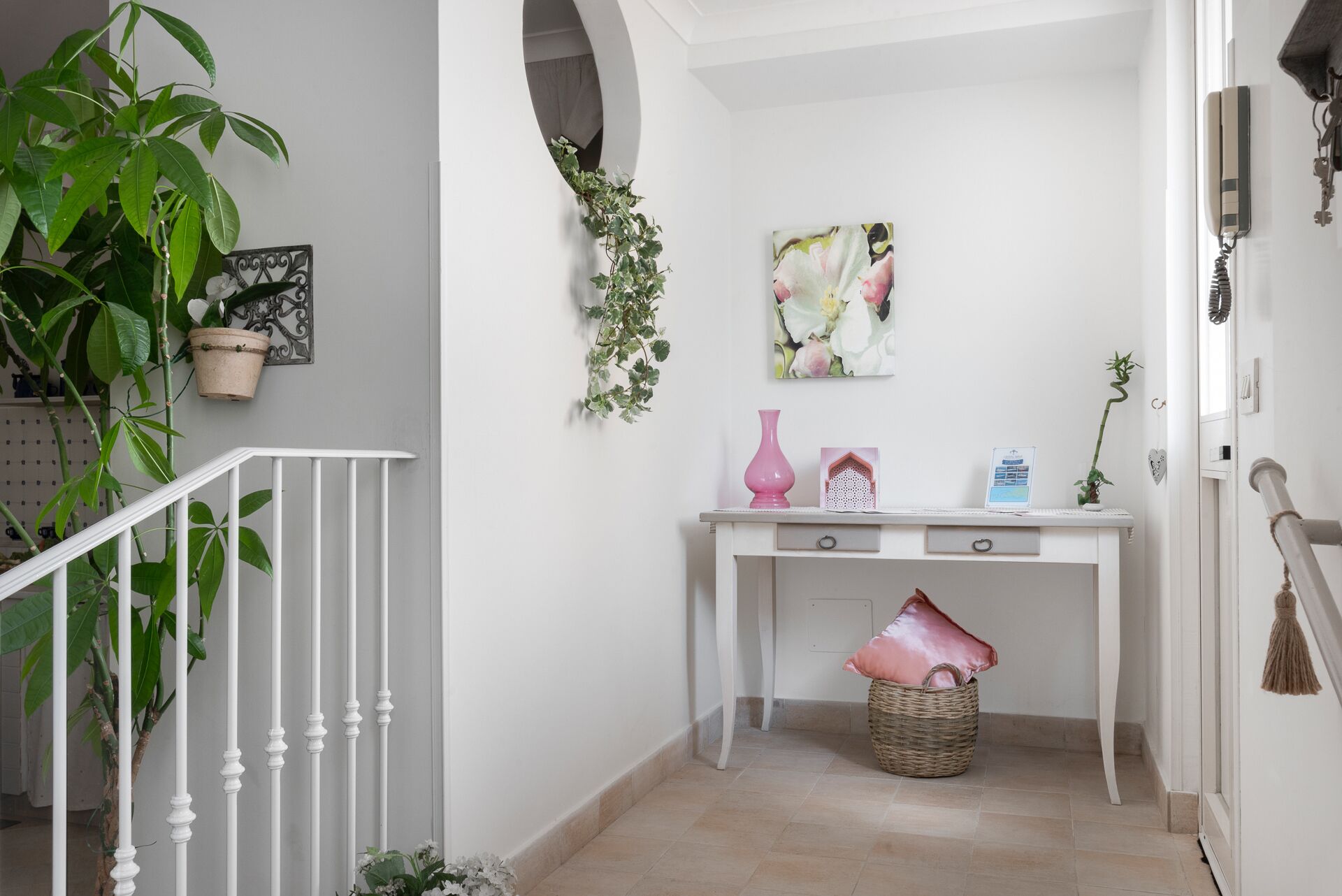 Ein weißes Konsolentischchen mit einer rosa Vase, einer kleinen Pflanze und einem gerahmten Bild.