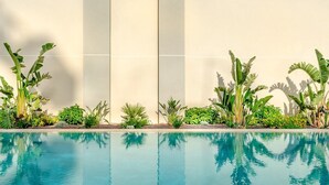 Une piscine à l’eau d’un bleu cristallin, entourée d’une végétation luxuriante et bordée d’un mur de couleur beige.