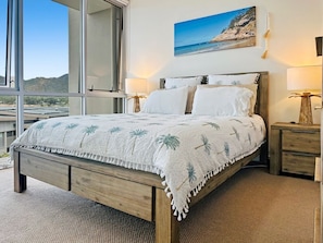 Una camera da letto con un letto, comodini, una lampada e un dipinto raffigurante una spiaggia.