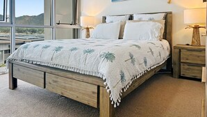 A bedroom with a bed, nightstands, a lamp, and a painting of a beach. - 1 Bright Point Apartment 1407 (Nelly Bay)
