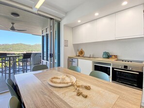 A modern kitchen with a dining area, a view of the outdoors, and a ceiling fan. - 1 Bright Point Apartment 1407 (Nelly Bay)