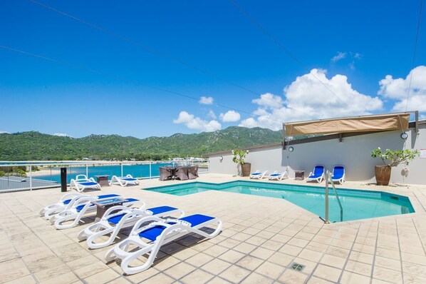 Une piscine sur le toit, dotée de chaises longues bleues, d’un espace salon couvert et offrant une vue sur la mer et les montagnes.