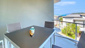 A balcony with a table and chairs, a view of the sea, and a building in the background. - 1 Bright Point Apartment 1407 (Nelly Bay)