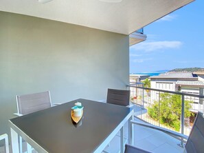 Ein Balkon mit Tisch und Stühlen, Blick auf das Meer und ein Gebäude im Hintergrund.