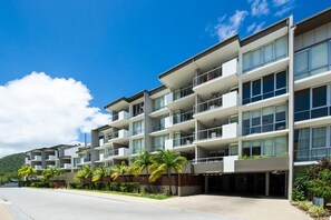 Un hôtel à plusieurs étages doté de balcons, de grandes fenêtres et d’un jardin paysager à l’avant, agrémenté de palmiers.