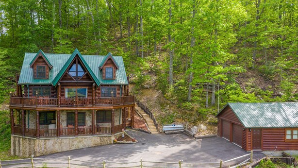 Une cabane en rondins dotée d’un balcon, avec des fondations en pierre et un toit en métal, entourée d’une forêt.