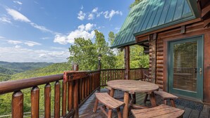 Une terrasse en bois avec une table ronde et des bancs, offrant une vue sur un paysage montagneux.