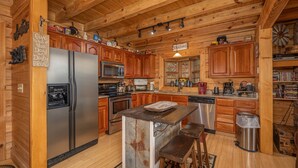Une cuisine rustique avec des meubles en bois, un réfrigérateur en acier inoxydable, un îlot central en bois avec des tabourets et un luminaire suspendu.