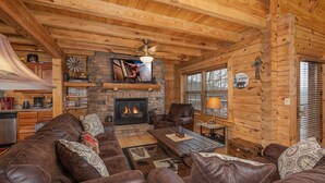 L’intérieur d’un chalet chaleureux, avec une cheminée, des canapés en cuir et des murs en bois.