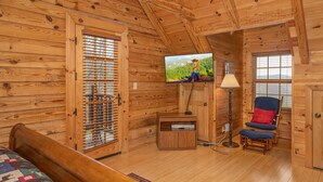 Une pièce de cabane en bois comprenant un lit, une télévision, une chaise et une fenêtre.
