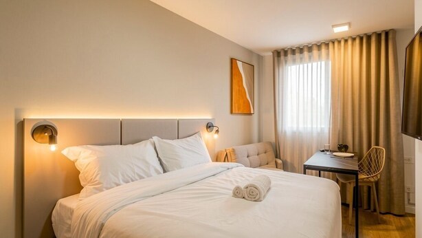 Ein Hotelzimmer mit Bett, Nachttisch, Stuhl und kleinem Schreibtisch mit Sitzgelegenheit.