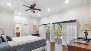 A bedroom with a bed, a ceiling fan, a desk with a lamp, and a view of the outdoors through a sliding door. - Maison Duffailly (Pompano Beach)