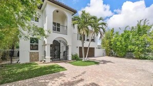 A two-story house with a white exterior, a gated entrance, and a paved driveway. - Maison Duffailly (Pompano Beach)