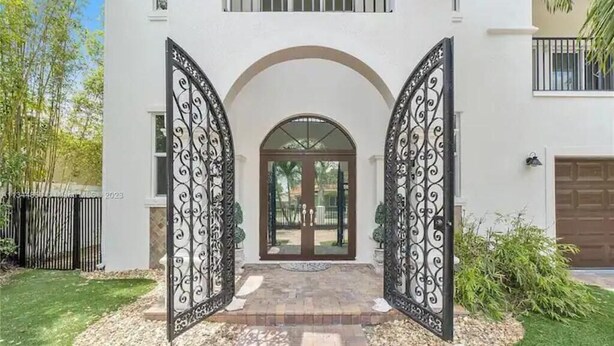 A two-story house with a white exterior, a front entrance with a glass door, and a driveway leading to a garage. - Maison Duffailly (Pompano Beach)