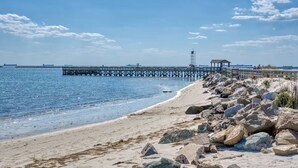 Una playa con costa rocosa, un muelle que se adentra en el agua y una pequeña construcción sobre el muelle.