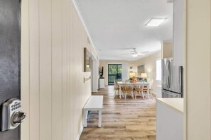 A hallway leading to a dining area with a table and chairs, a bench, and a refrigerator.
