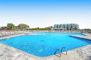 A swimming pool with multiple lanes, surrounded by lounge chairs and a building with balconies.