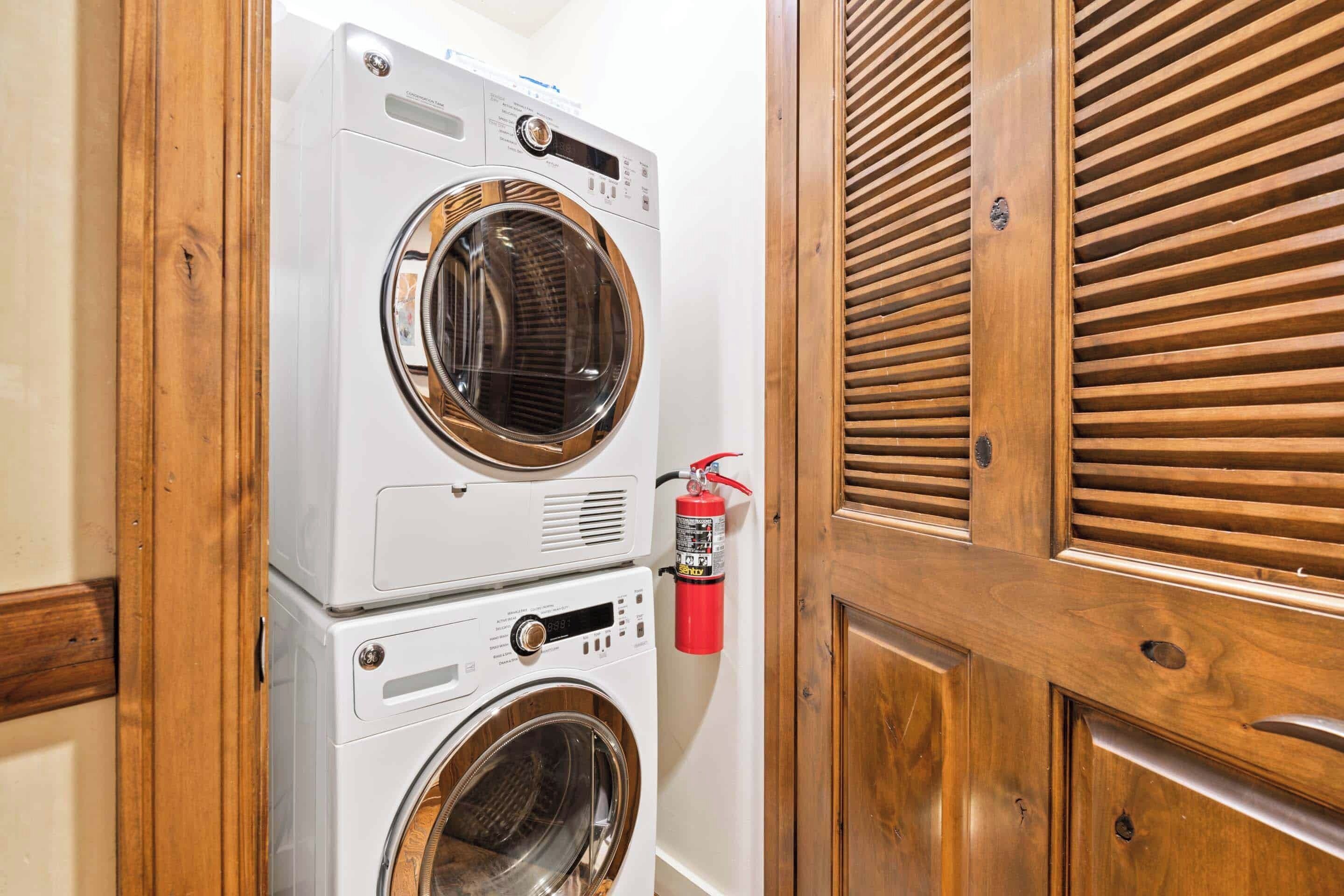A laundry area with stacked washing machines and a fire extinguisher mounted on the wall.