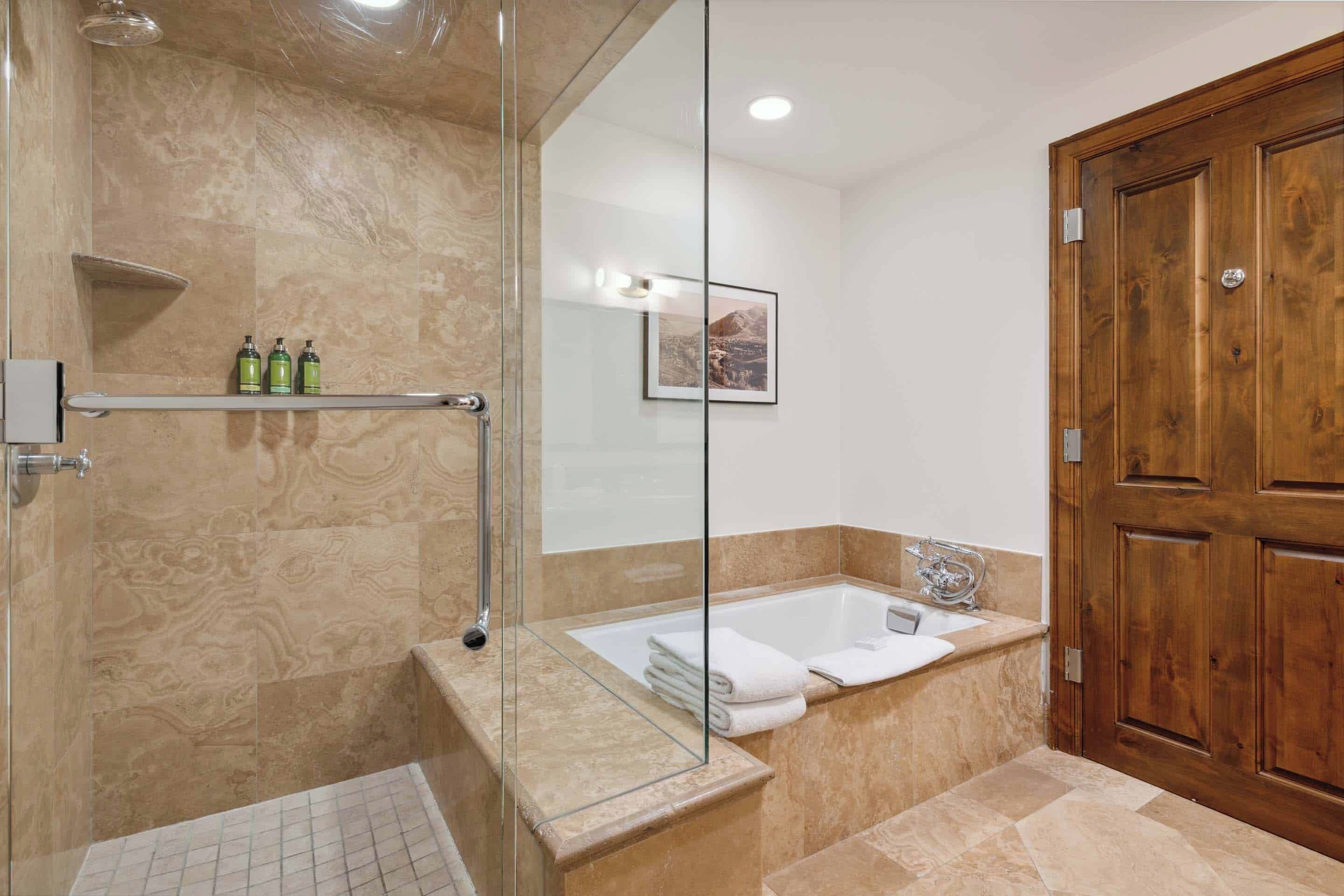 Un baño moderno con cabina de ducha de vidrio, una bañera independiente y una puerta de madera.