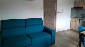 Ein Zimmer mit einem türkisfarbenen Sofa, einer Holztür, einer Küche mit Schränken und einer Klimaanlage.