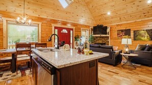 A wooden cabin interior with a kitchen, dining area, and living room. - Beary Cozy Den (Gatlinburg)