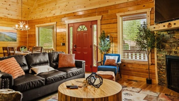 A cozy log cabin interior with a leather sofa, a round coffee table, and a fireplace. - Beary Cozy Den (Gatlinburg)