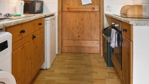 A kitchen with wooden cabinets, a microwave, a dishwasher, and a wooden door with a towel hanging on it. - UK46717 - The Orchard (Plumstead Green, near Holt)