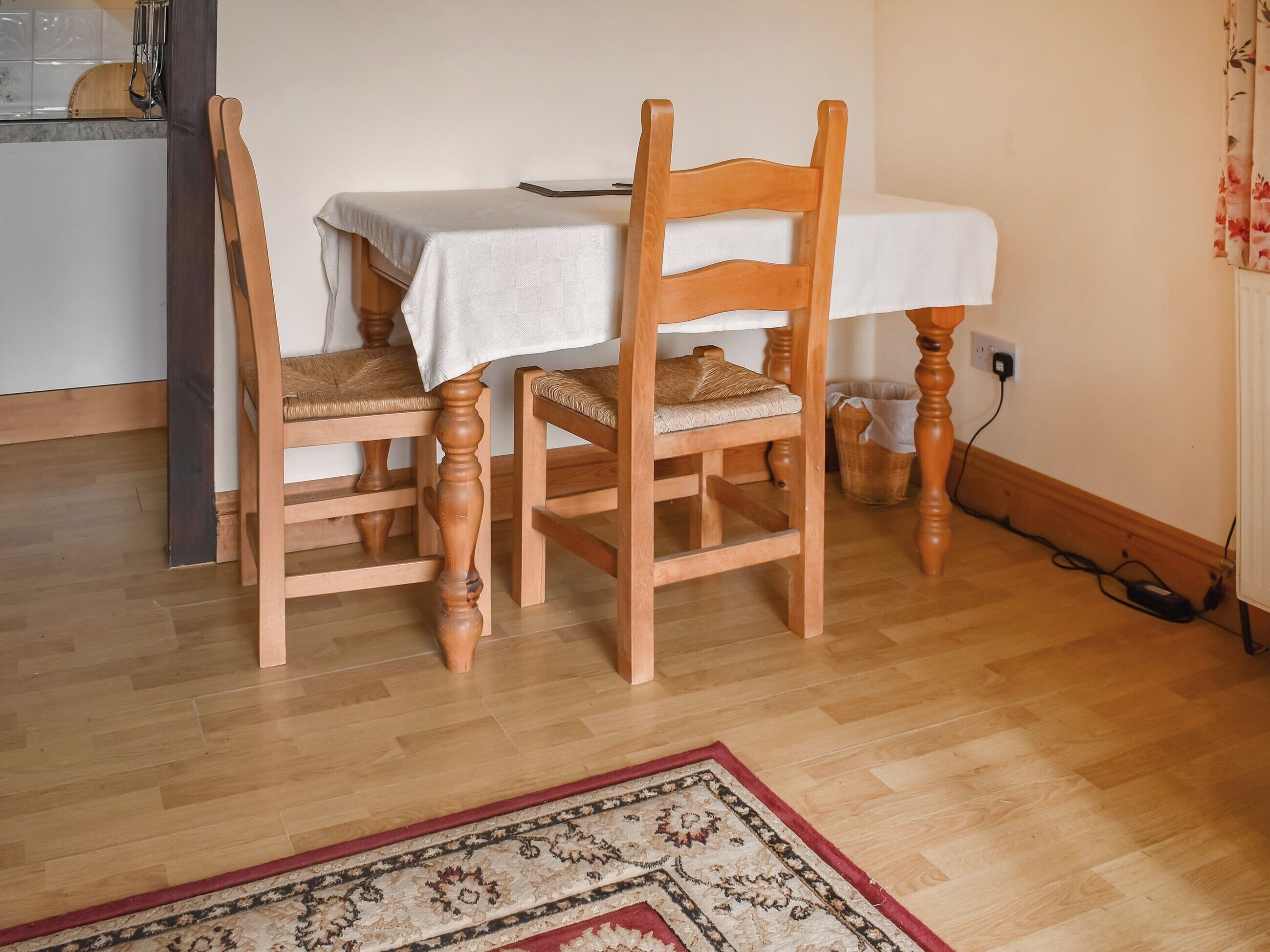 Un comedor con una mesa y sillas de madera, un tapete estampado y una cocina al fondo.