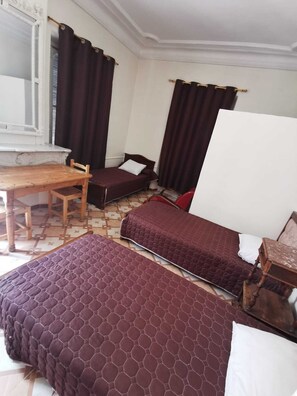 A room with two beds, a wooden table, and a window with curtains. - Grand Hotel Moderne - Port d'Alger (Algiers)